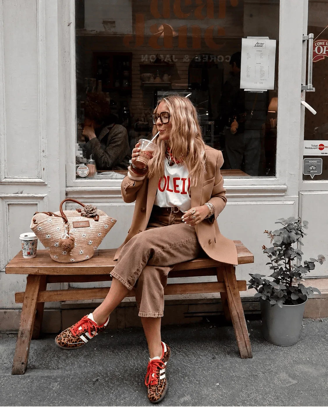 Creator sentada em banco com blazer caramelo e tênis estampados
