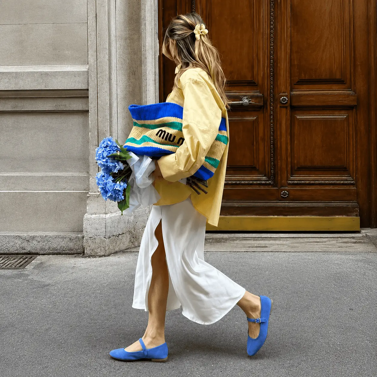 Creator vestindo blusa amarela e segurando bolsa MiuMiu azul em rua europeia